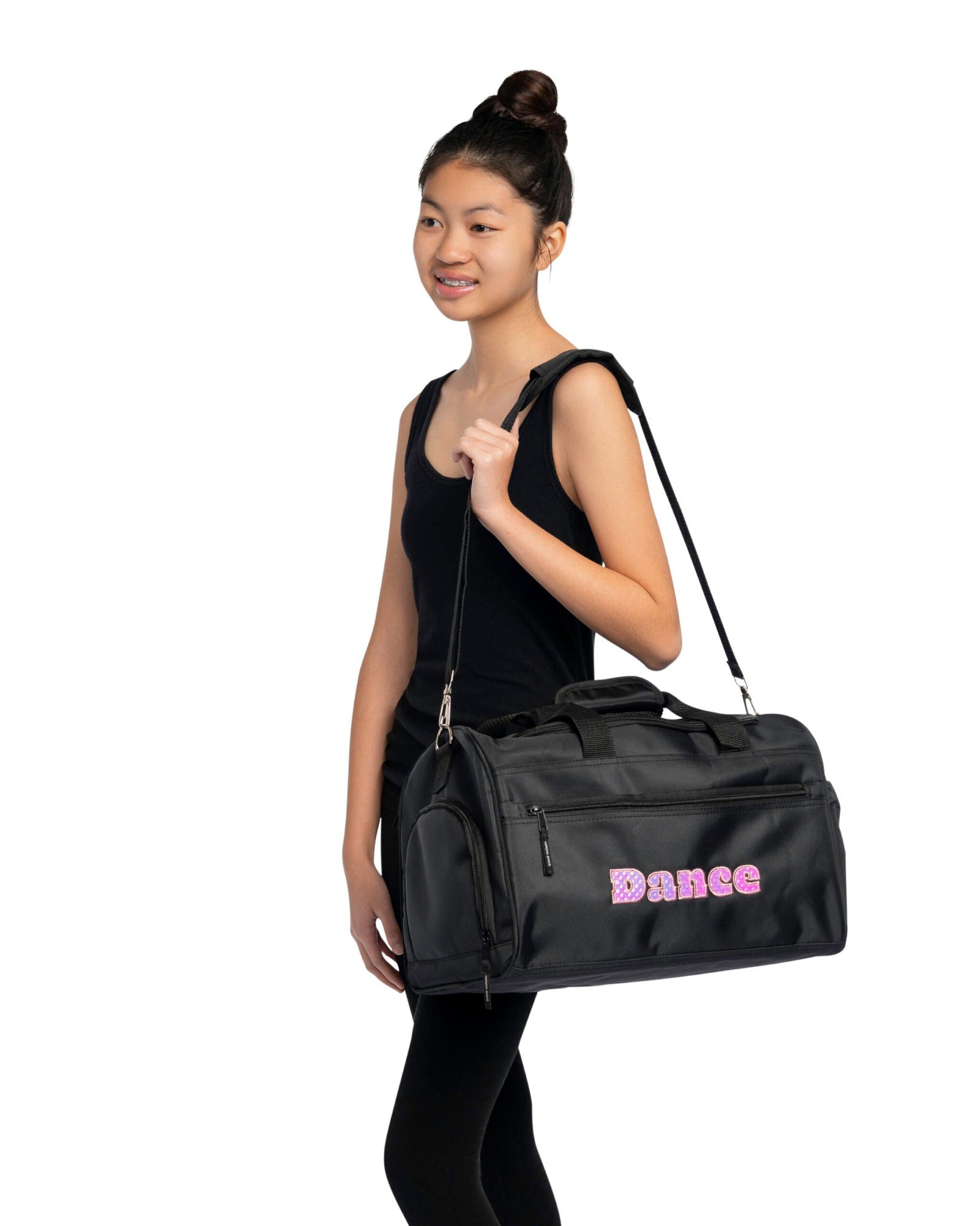 A woman wearing a black tank top and leggings carries a black duffel bag with pink 'Dance' lettering on the front, set against a plain white background.