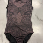 A sleeveless leotard with a dark brown and black abstract floral lace-like pattern, laid flat on a white marble surface.
