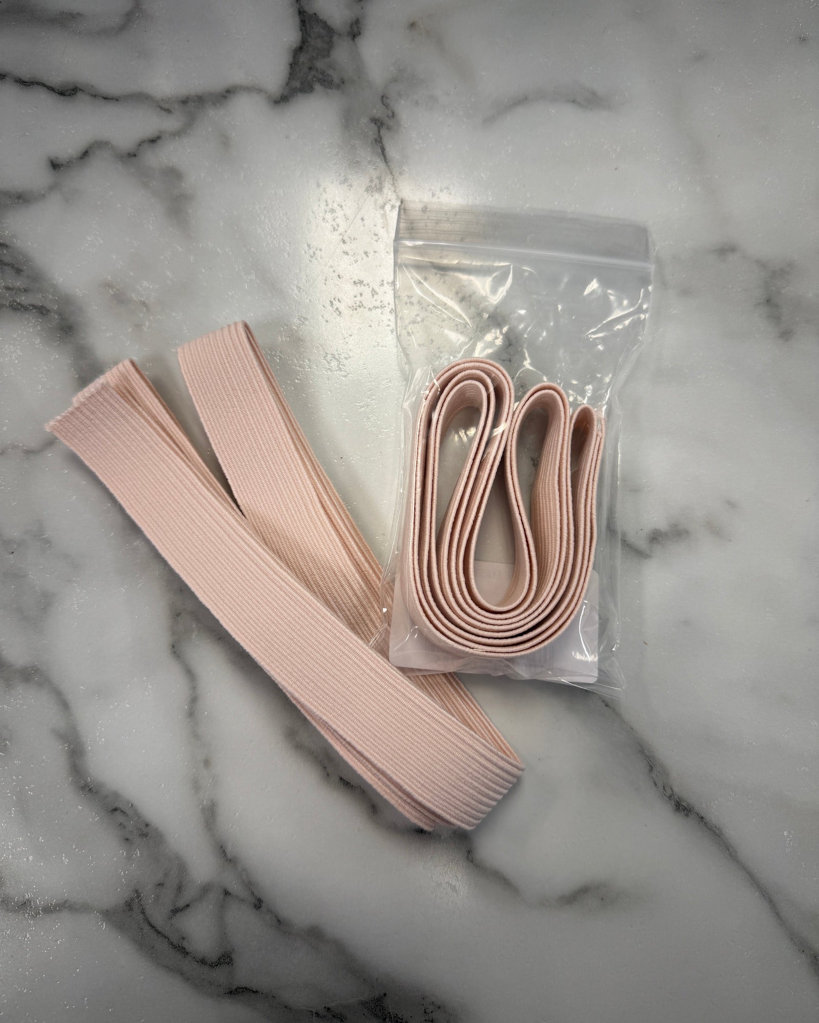 Pink elastic bands on a marble surface with a clear plastic bag containing more bands.