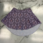 A purple fabric pull on skirt with a repeating white scroll and star pattern, laid flat on a white and gray marble surface.