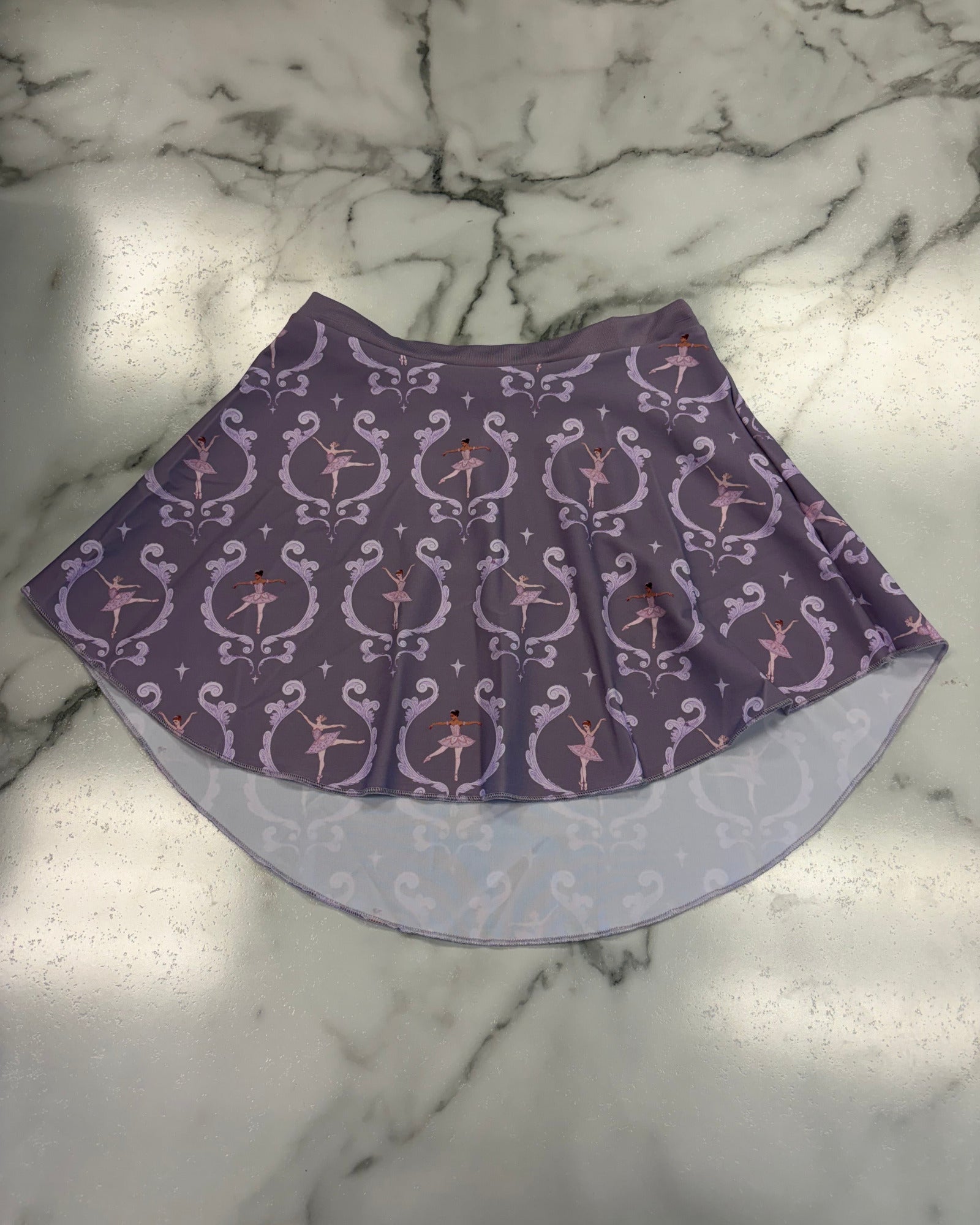 A purple fabric pull on skirt with a repeating white scroll and star pattern, laid flat on a white and gray marble surface.