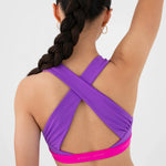 A woman shown from the back wearing a purple bra top with a bright pink underband and matching purple shorts. The brand name 'every turn' is visible subtly on the underband of the sports bra.