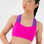 A woman modeling a bright pink and purple bra top and matching purple shorts against a light gray studio background.