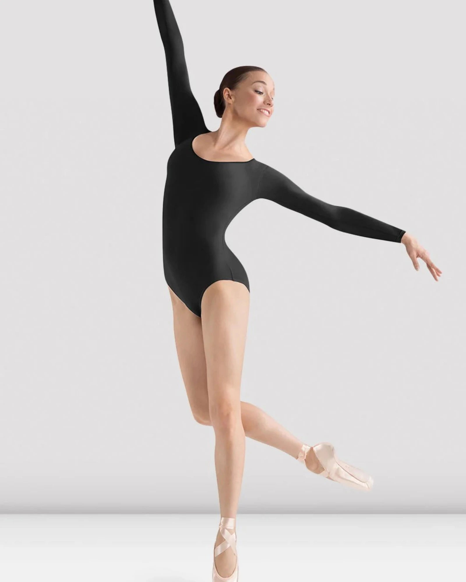 Ballerina in a black long sleeve  leotard and pink ballet shoes posing against a white background.