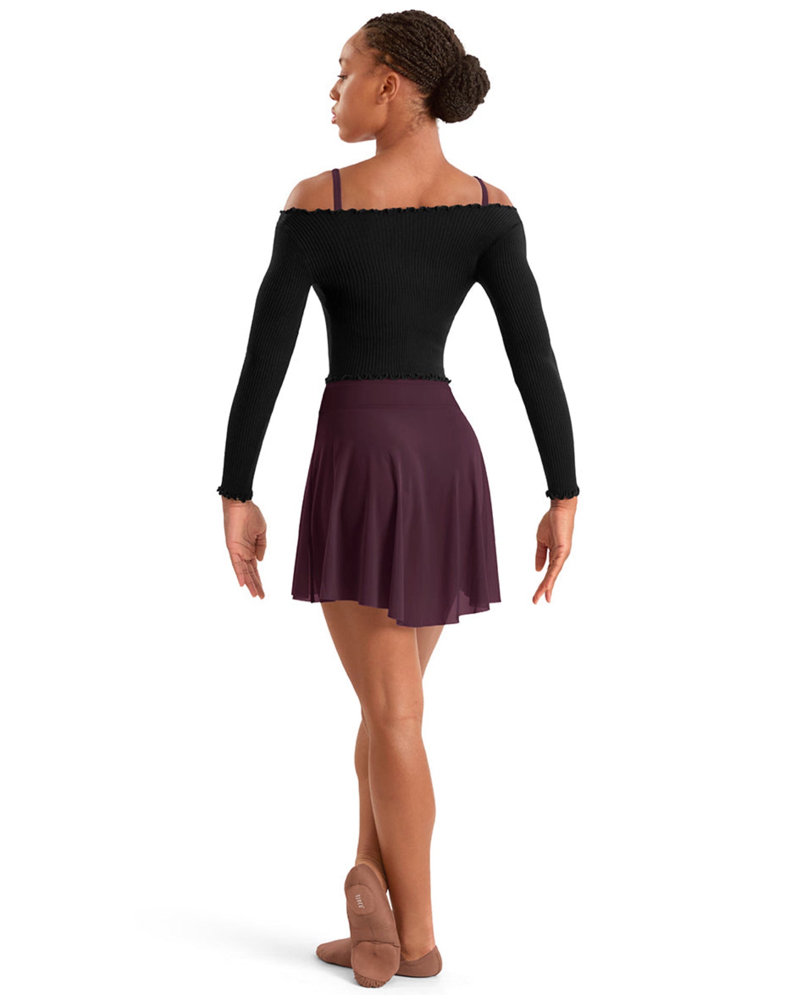 A woman modeling a black long-sleeve off-the-shoulder dance leotard and a dark plum pleated mini skirt, shown from the back against a solid white background.