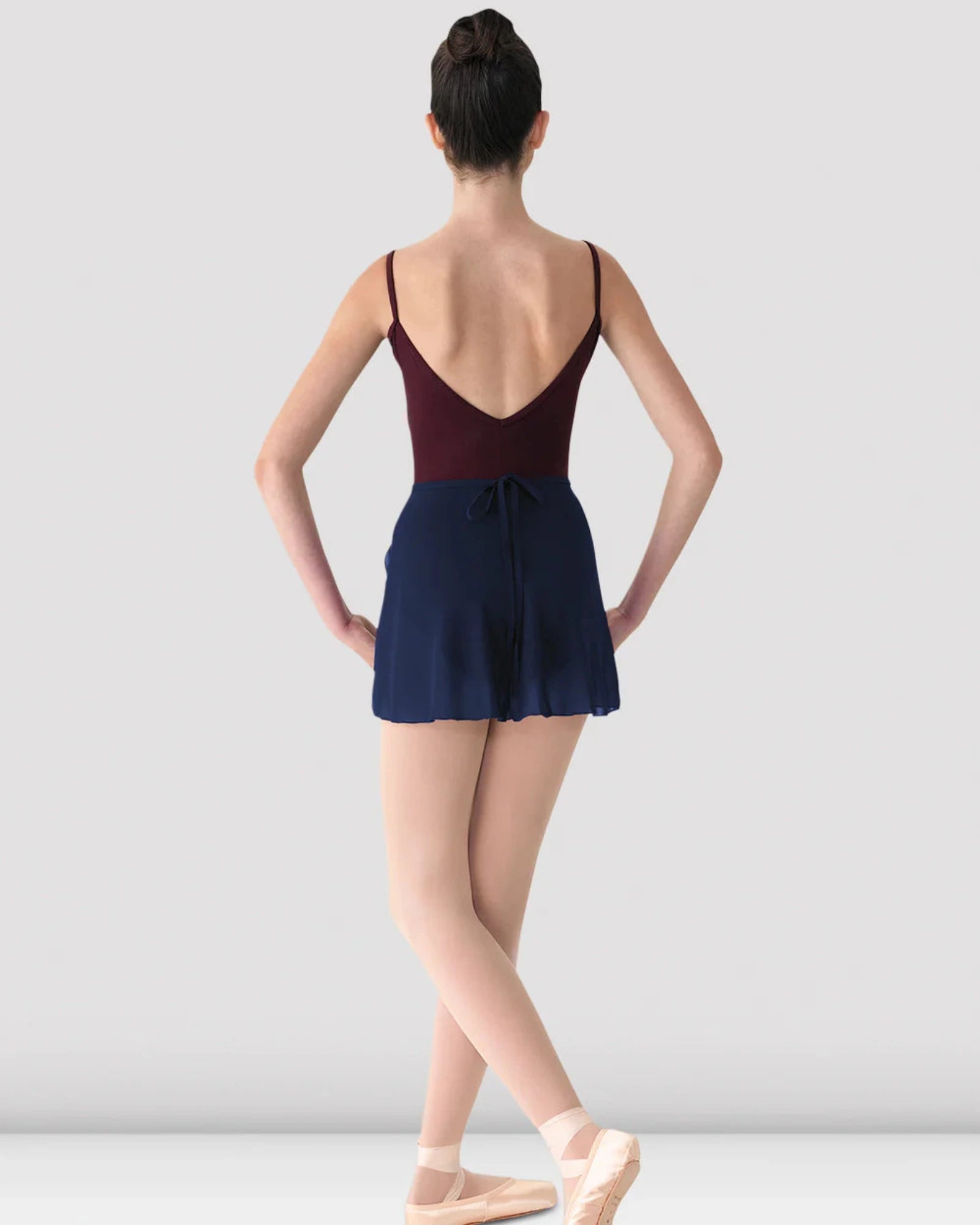 Ballerina in a maroon leotard and navy skirt on a white background