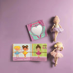A children's dance-themed gift set arranged on a lavender background, including a small illustrated book with ballerina illustrations, a heart-shaped mirror in a pink sleeveless case, and two fabric ballerina dolls in pastel outfits.