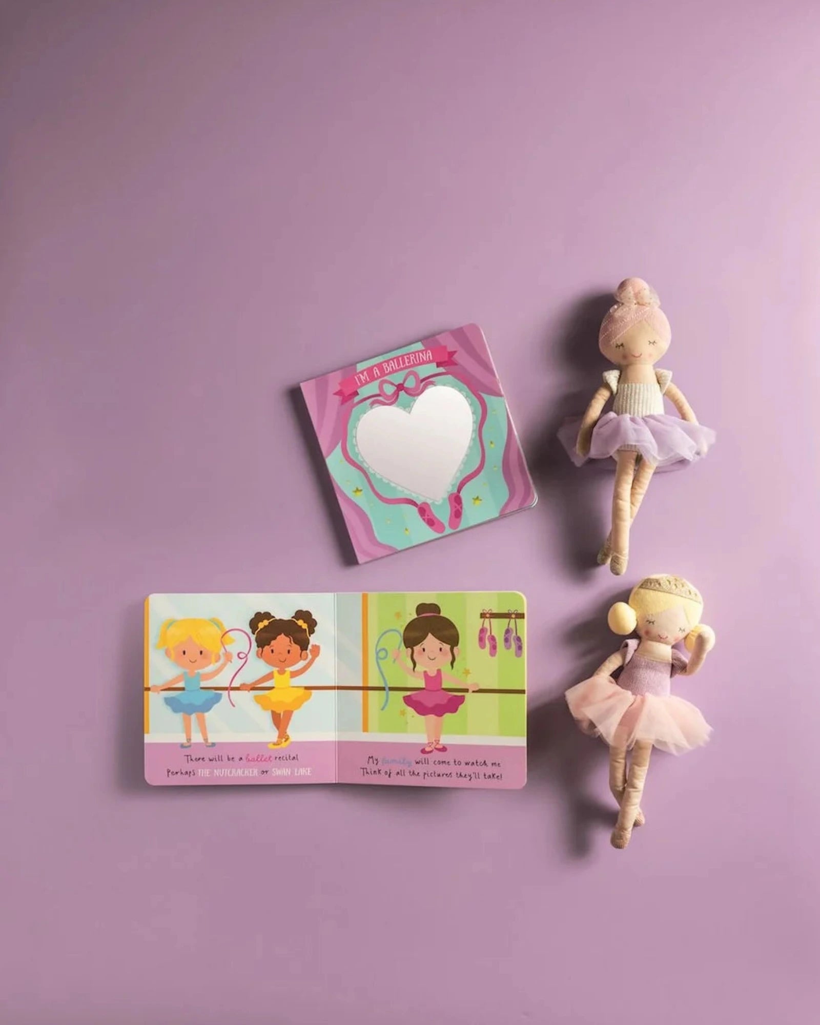 A children's dance-themed gift set arranged on a lavender background, including a small illustrated book with ballerina illustrations, a heart-shaped mirror in a pink sleeveless case, and two fabric ballerina dolls in pastel outfits.