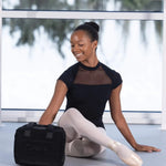 Ballerina sitting on the floor with a black bag in a ballet studio.