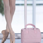 Person wearing ballet shoes with a pink ballet bag on a light surface.