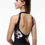 A woman shown from the back wearing a black leotard with a floral print on the lower back and sides, photographed against a clean white studio background.