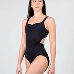 A woman modeling a black leotard with a square neckline, ruched bust, and side cutouts, photographed against a light gray studio background.