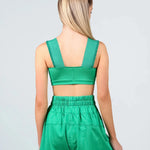 A woman shown from the back wearing a matching green two-piece dance outfit consisting of a crop top and high-waisted shorts, against a light gray studio background.