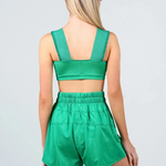 A woman shown from the back wearing a matching green two-piece dance outfit consisting of a crop top and high-waisted shorts, against a light gray studio background.
