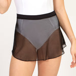A model wearing a sheer mesh dance skirt in black, layered over a white bodysuit, shown from the waist to the upper thighs against a light studio background.