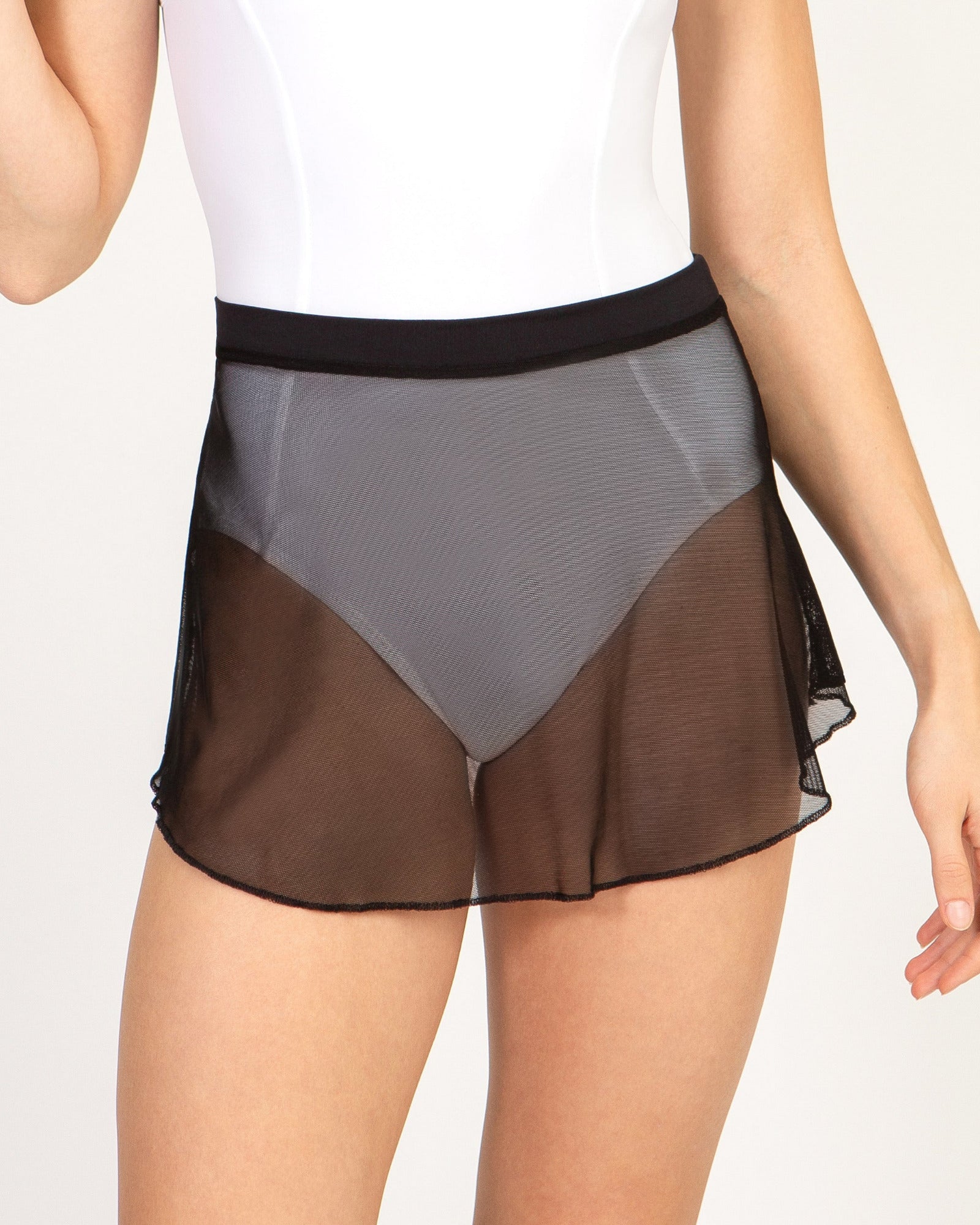 A model wearing a sheer mesh dance skirt in black, layered over a white bodysuit, shown from the waist to the upper thighs against a light studio background.