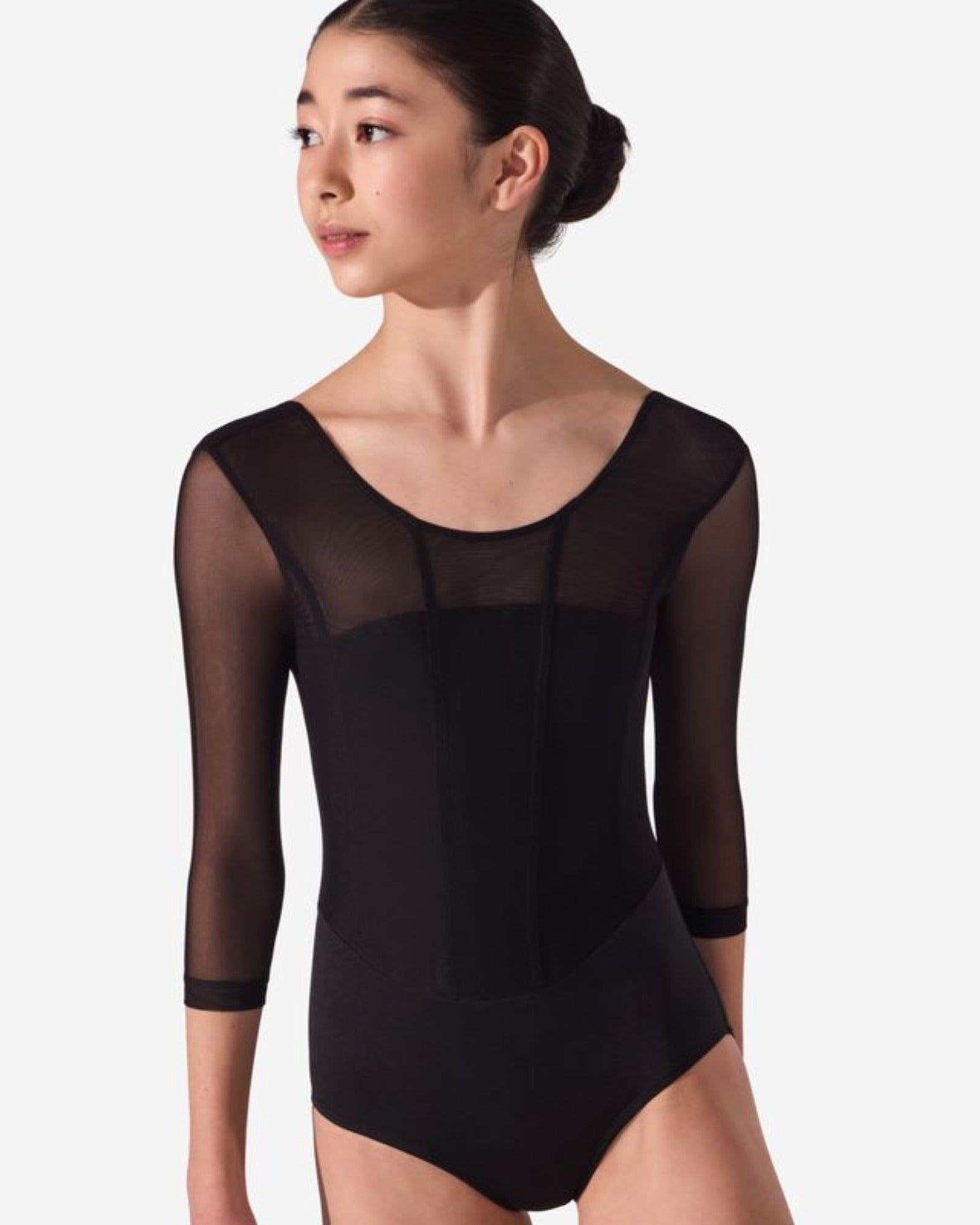 A young female dancer wearing a black three-quarter sleeve leotard with sheer mesh sleeves, shown from the waist up against a light gray studio background.
