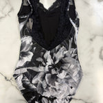 A black and white floral print one-piece leotard with a black lace V-neck bodice, laid flat on a white marble surface.
