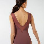 A woman shown from the back wearing a sleeveless leotard in a muted dusty rose or mauve color with sheer mesh paneling at the back, photographed against a clean light gray studio background.