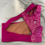A bright pink dance bra with a shiny holographic mesh back panel and a peach-colored lining, laid flat on a white marble surface.
