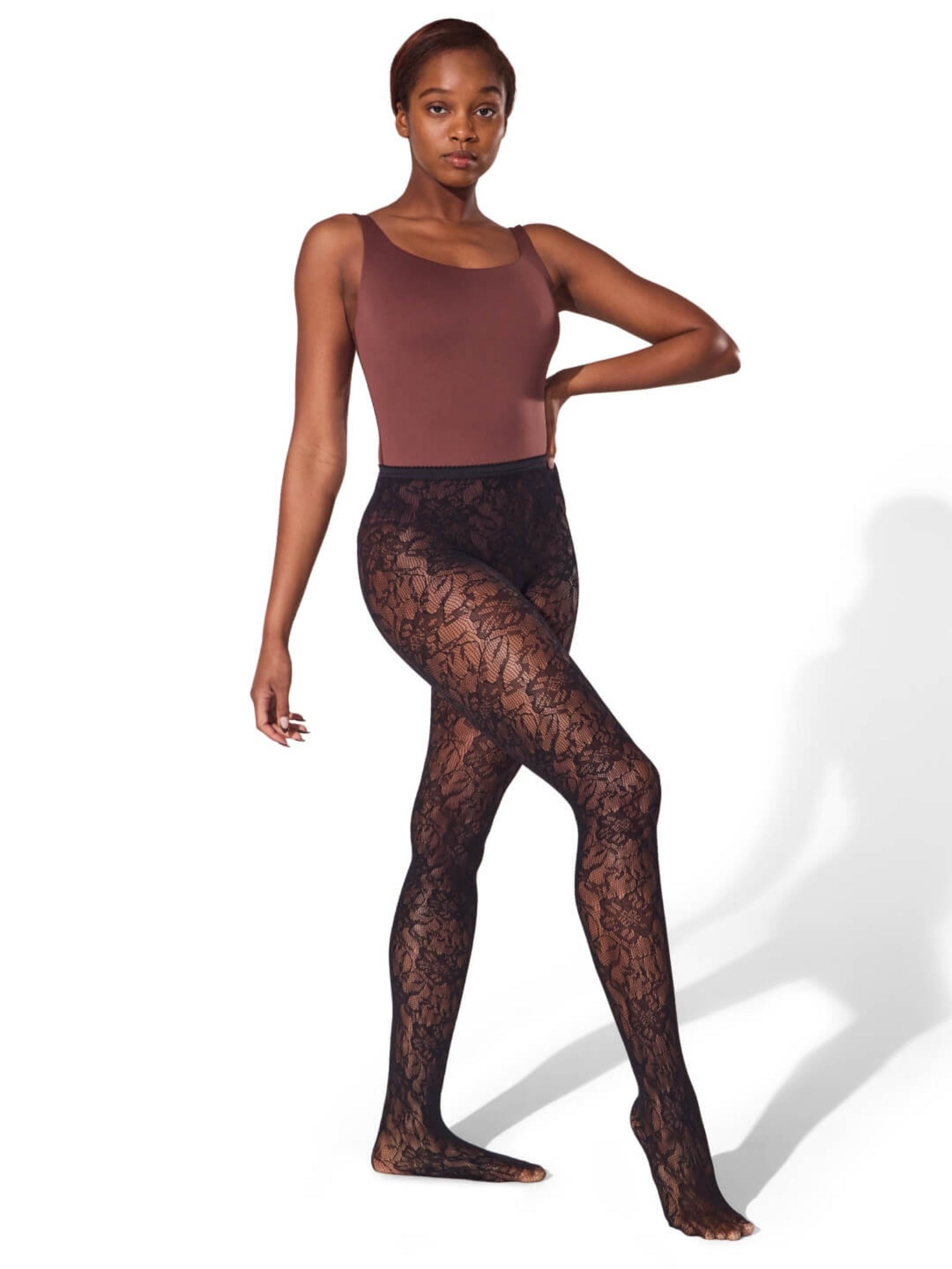 Model wearing brown bodysuit and black lace tights on a white background