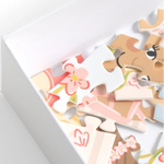 A close-up of a white box containing colorful puzzle pieces with a cartoon animal face and floral designs, photographed on a clean white background.