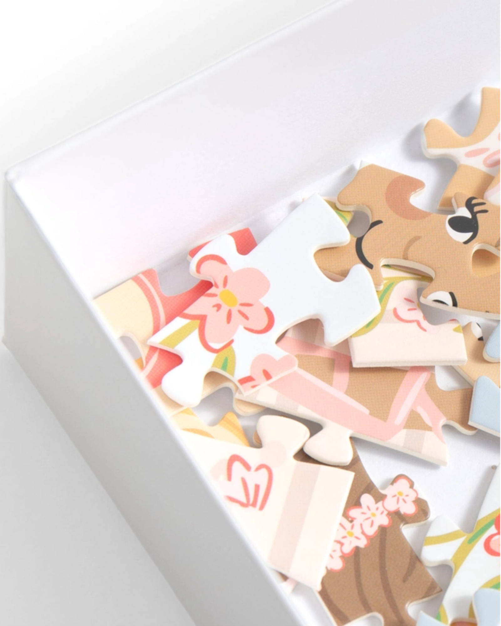 A close-up of a white box containing colorful puzzle pieces with a cartoon animal face and floral designs, photographed on a clean white background.