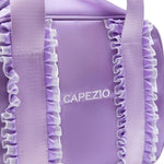 A close-up of a lavender purple dance bag with ruffled trim and wide shoulder straps, featuring the brand name 'CAPEZIO' printed in white on the front.