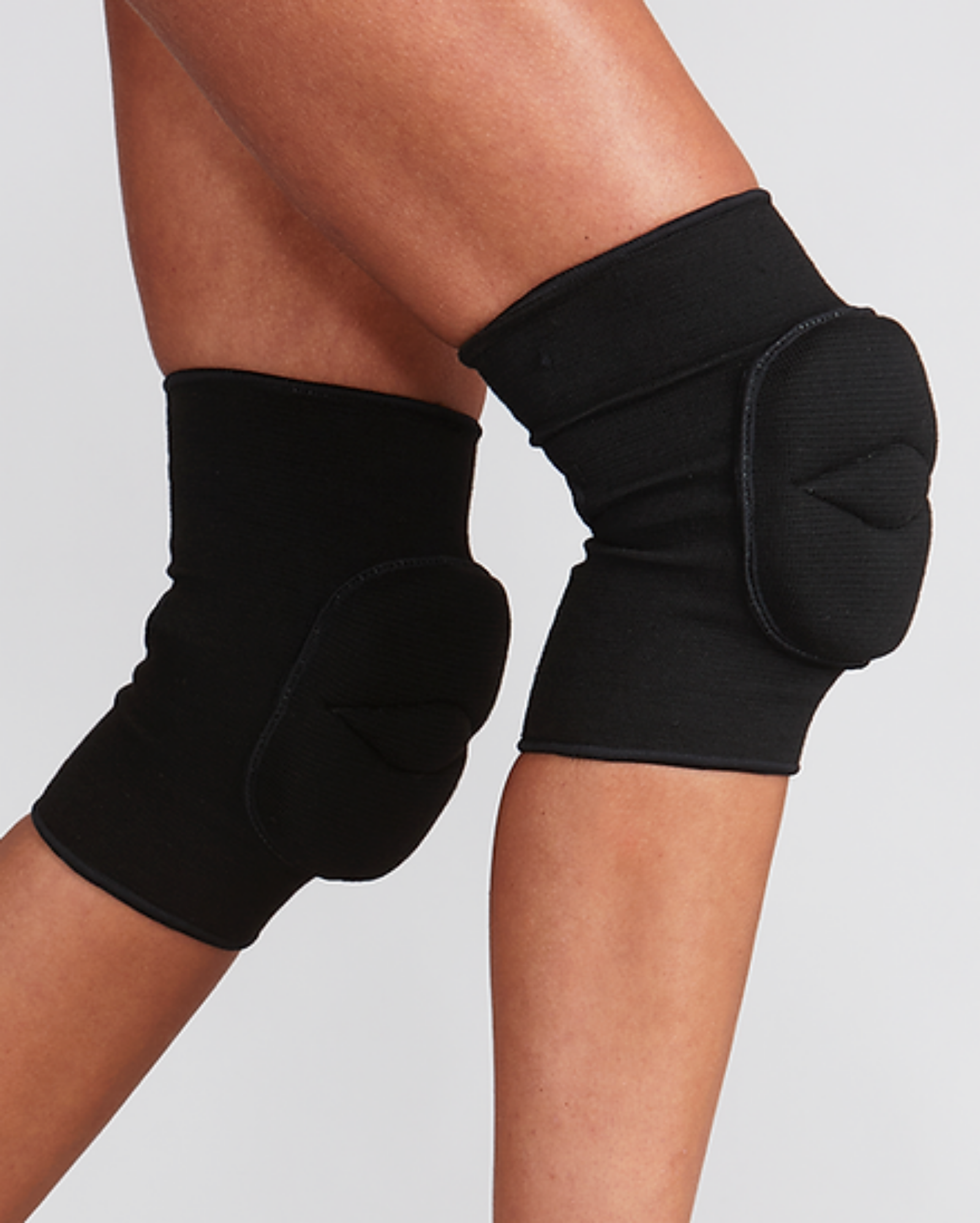 Black knee pads on a person's legs against a light gray background