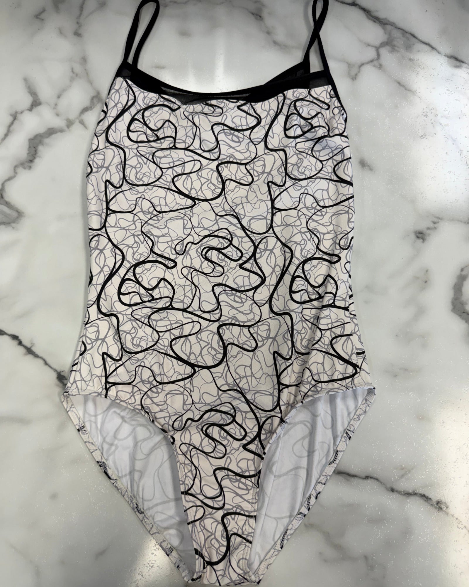 A leotard with a black and white abstract line pattern, laid flat on a white and gray marble surface.