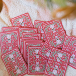 A pile of red patterned cards or envelopes featuring white cartoon characters and green leaf motifs, arranged on a soft beige fabric background.