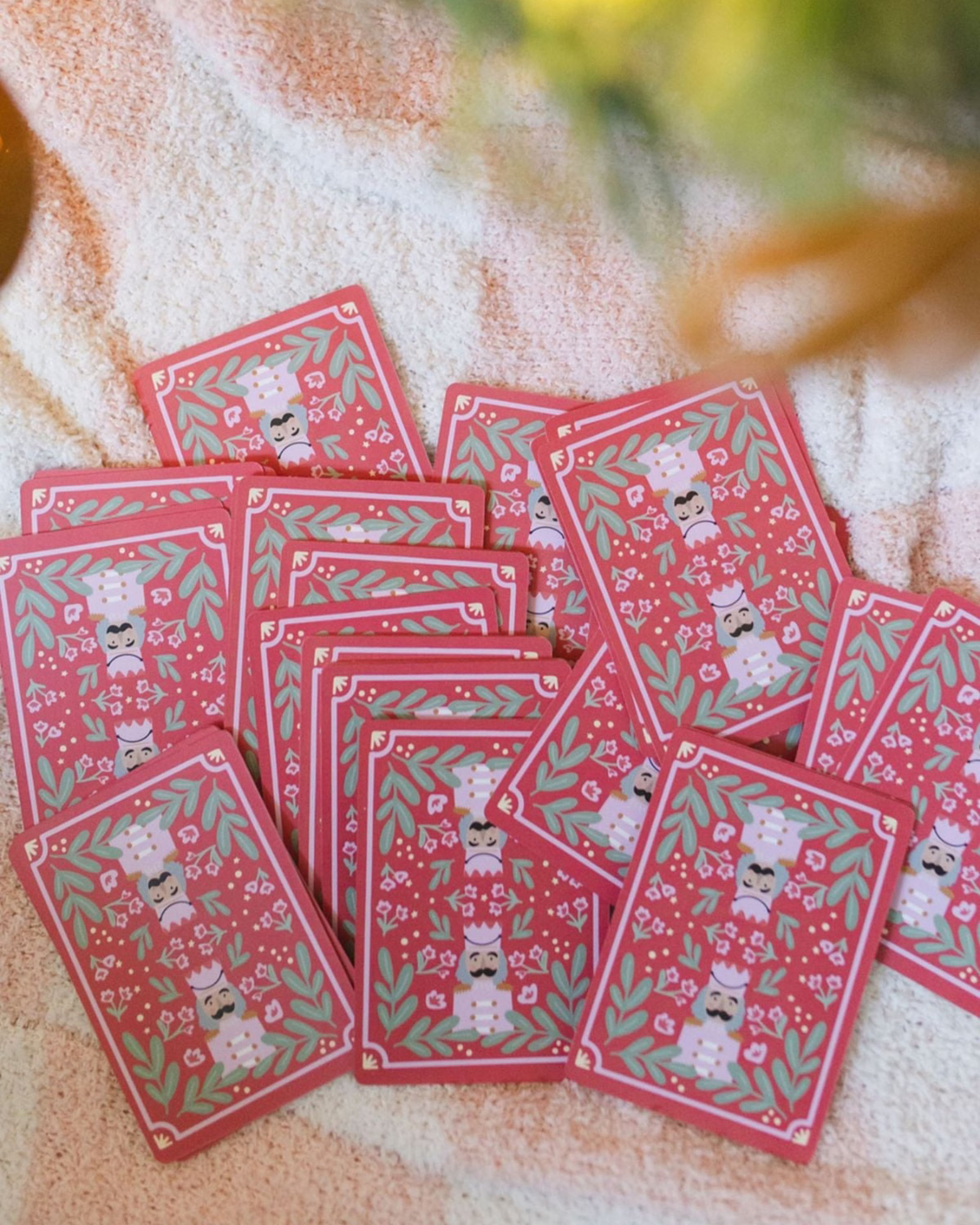 A pile of red patterned cards or envelopes featuring white cartoon characters and green leaf motifs, arranged on a soft beige fabric background.