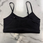 A black bra top with thin straps and a textured, dotted fabric pattern, laid flat on a white marble surface.