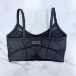 A dark gray mesh and structured sports bra with geometric paneling and a small 'CH LA LA' brand label on the front, laid flat on a white marble surface.