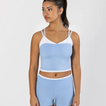 A woman modeling a light blue and white two-piece dancewear set, consisting of a cropped camisole top and matching high-waisted shorts, against a plain light gray background.