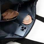 Black bag with a phone, tan tights, and pink ballet slippers inside on a white background