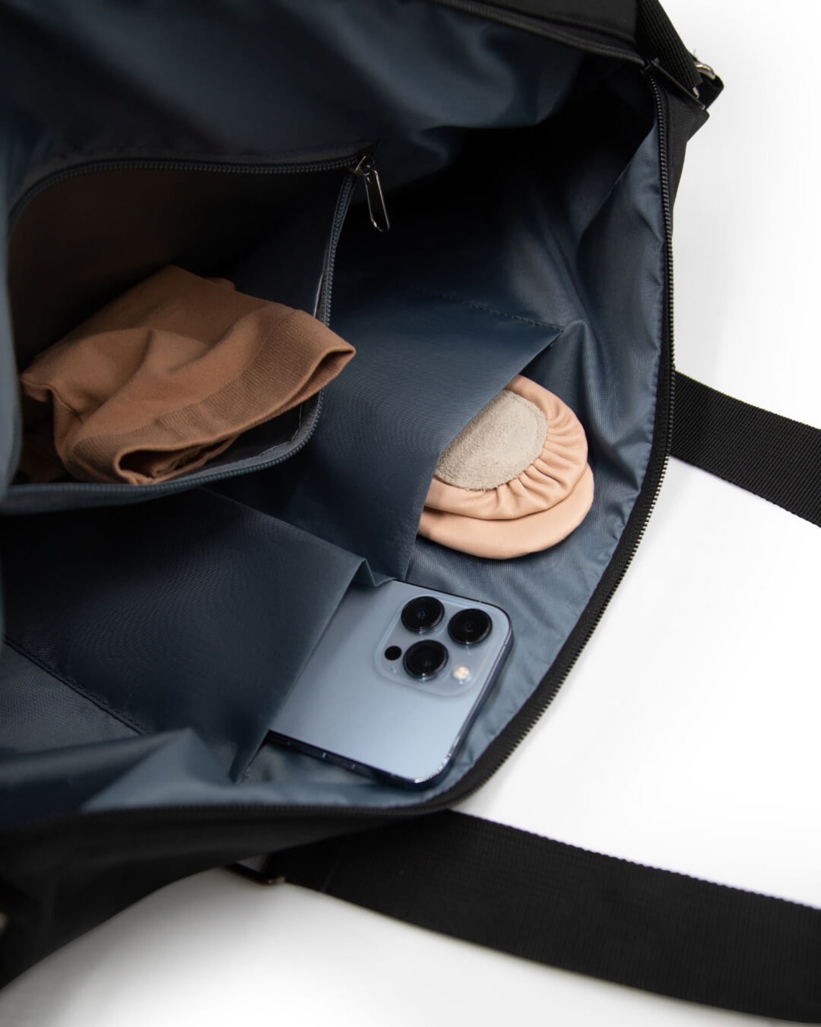 Black bag with a phone, tan tights, and pink ballet slippers inside on a white background