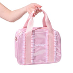 A pink shiny dance bag with satin handles and pleated trim, held by a person's hand against a white background.