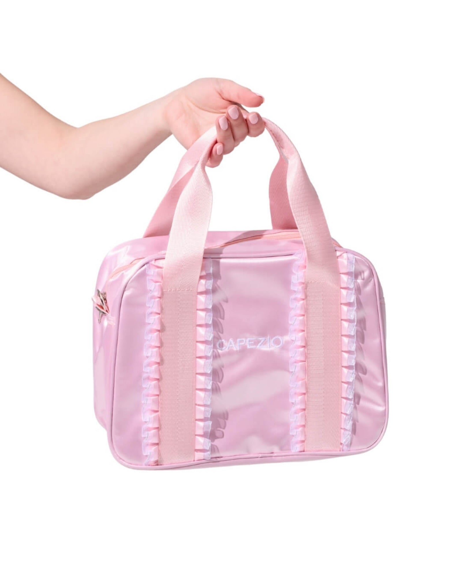 A pink shiny dance bag with satin handles and pleated trim, held by a person's hand against a white background.