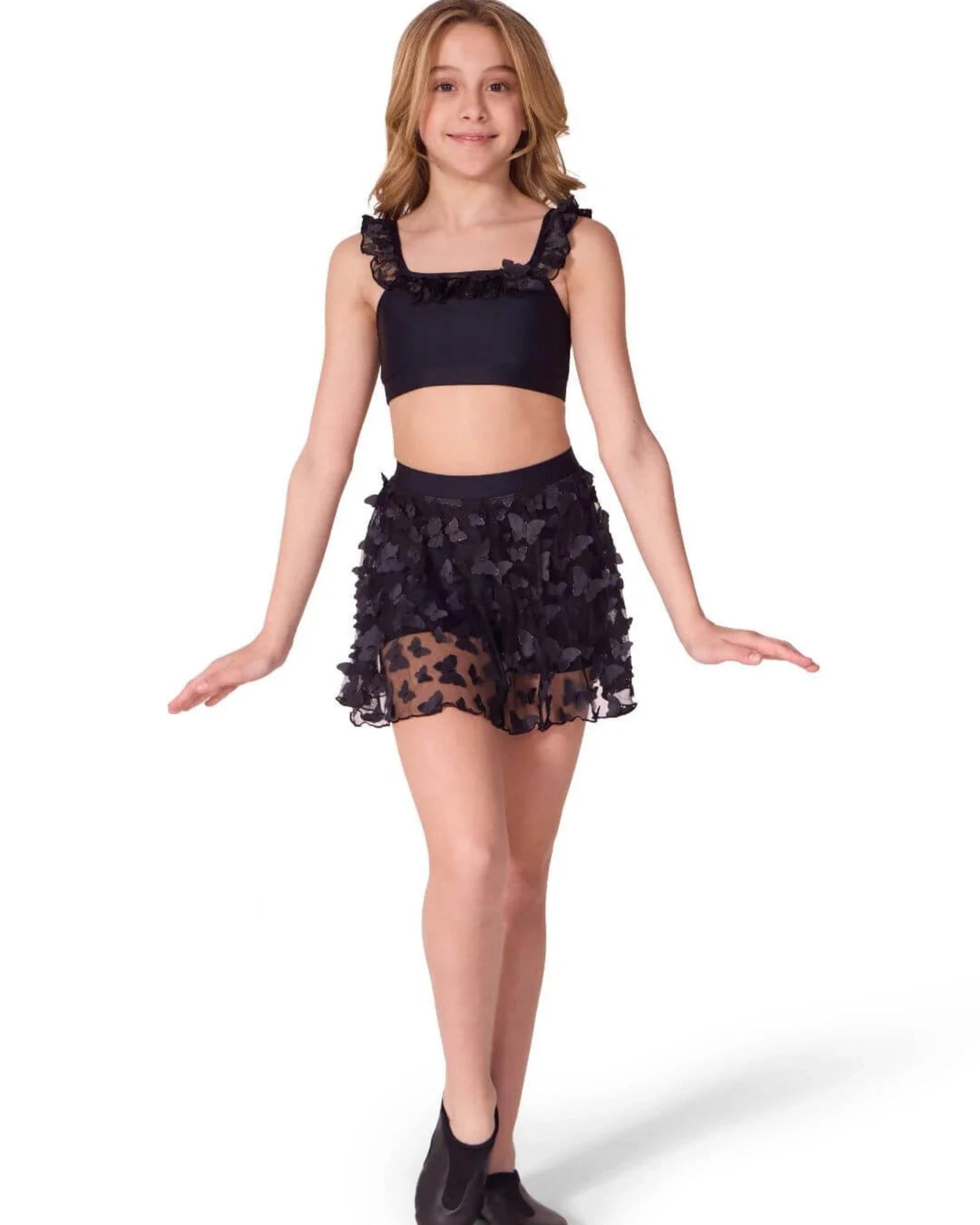 Young girl wearing a black dance outfit with ruffled top and skirt on a white background