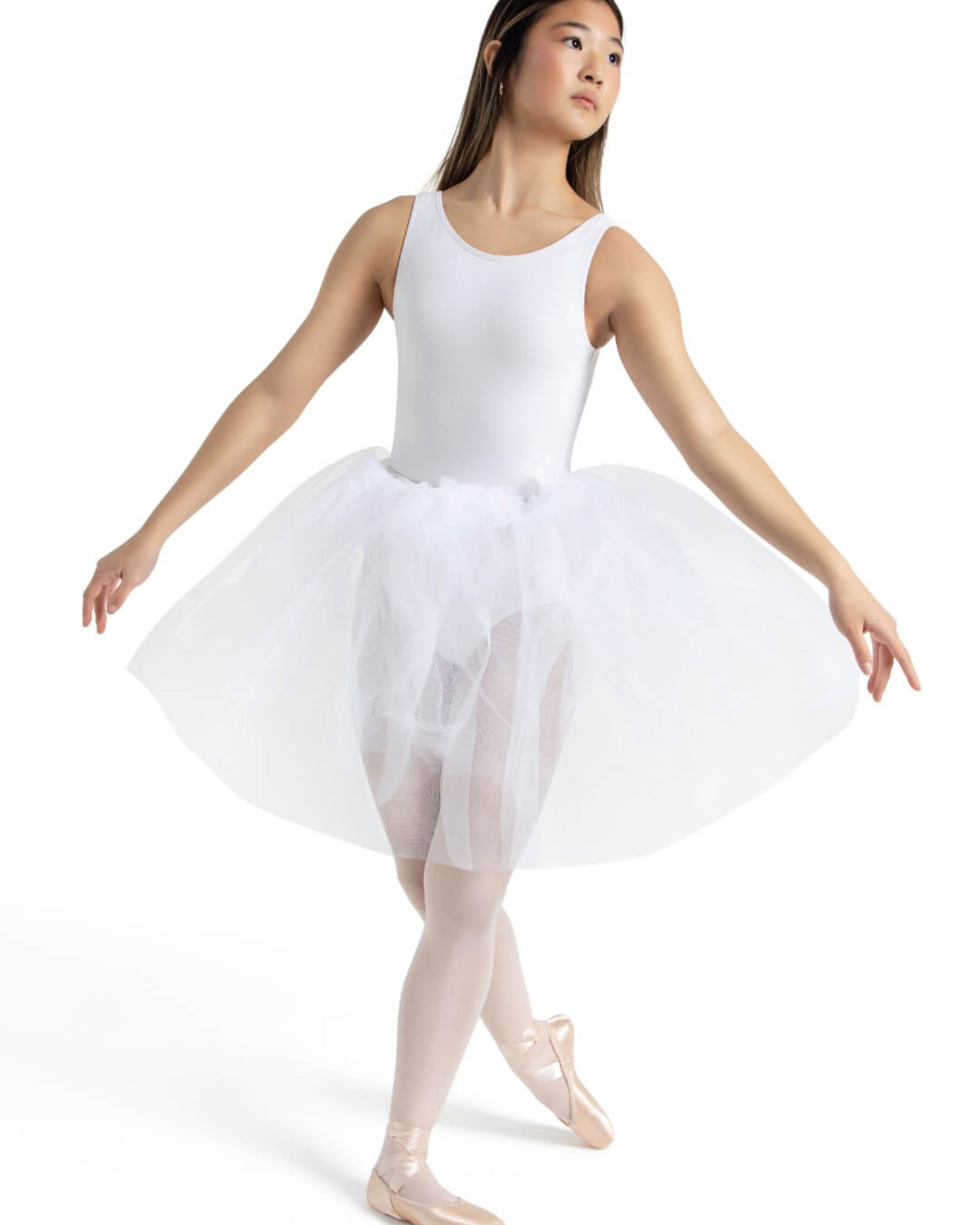 A young ballerina model wearing a white sleeveless leotard, a voluminous white tulle tutu skirt, and light pink pointe shoes, posed against a solid white studio background.