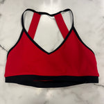 A red crop top with black trim and a crossover back strap design, laid flat on a white marble surface.