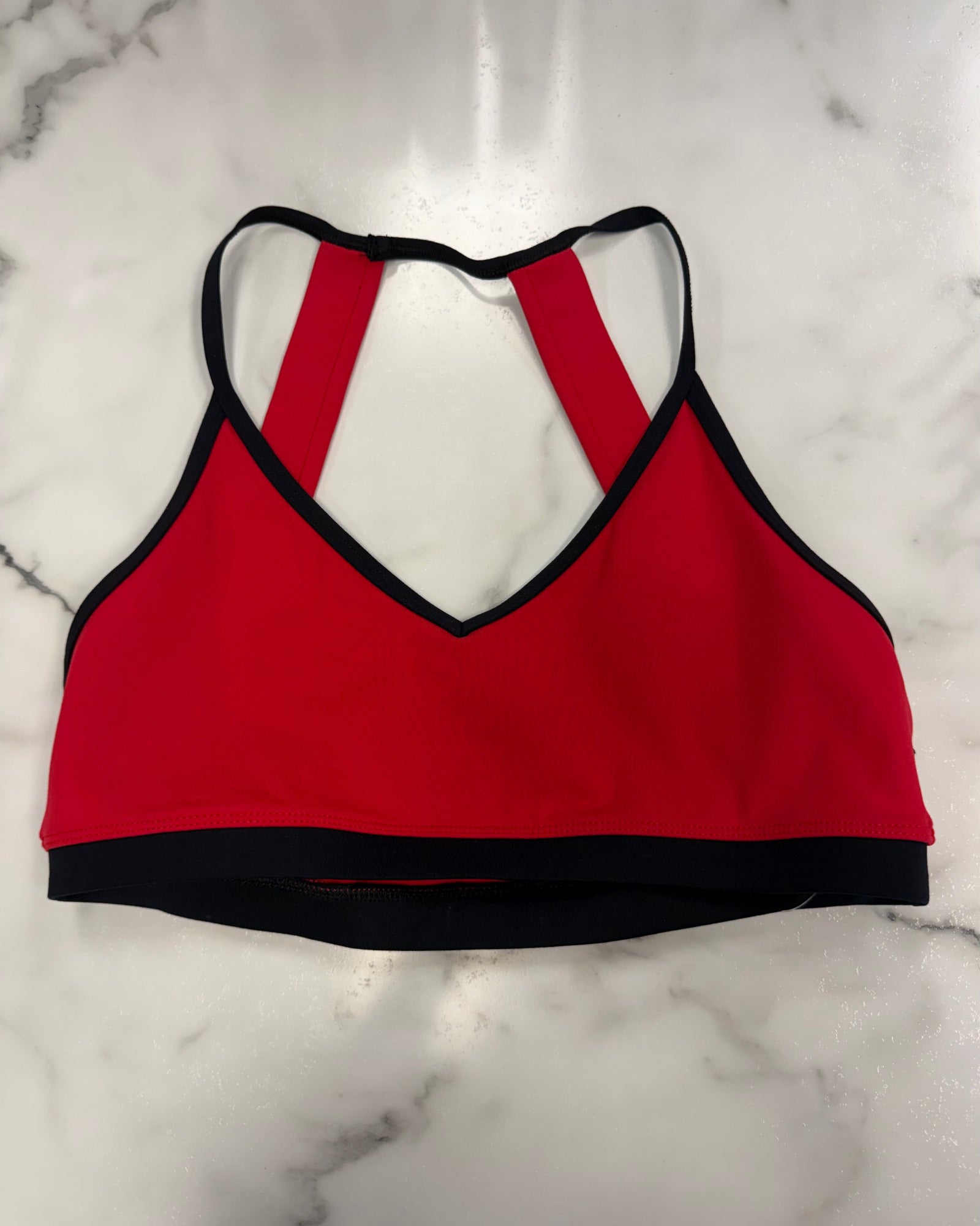 A red crop top with black trim and a crossover back strap design, laid flat on a white marble surface.