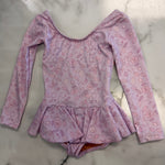 A long-sleeve baby/toddler leotard dress in light pink with a darker pink leaf pattern, laid flat on a white marble surface.