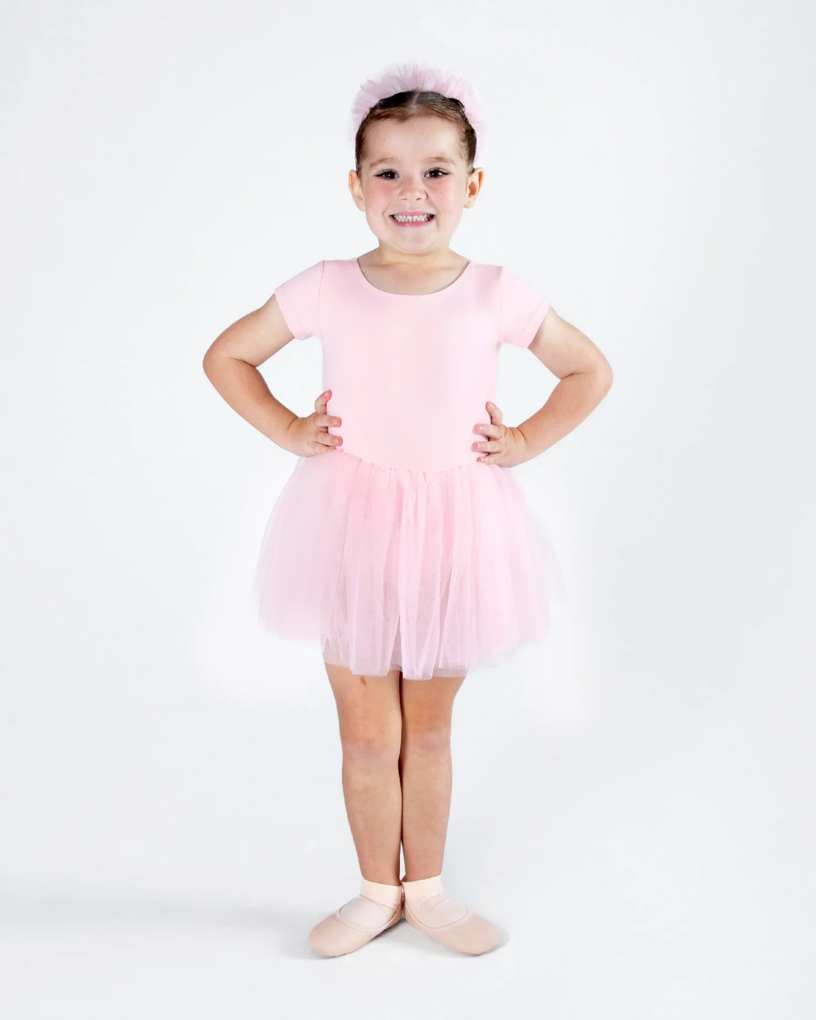 Young girl in a pink ballet outfit posing on a white background