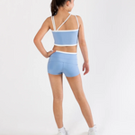 A girl modeling a light blue activewear set consisting of a dance bra and matching shorts, shown from a rear three-quarter view against a plain white studio background.