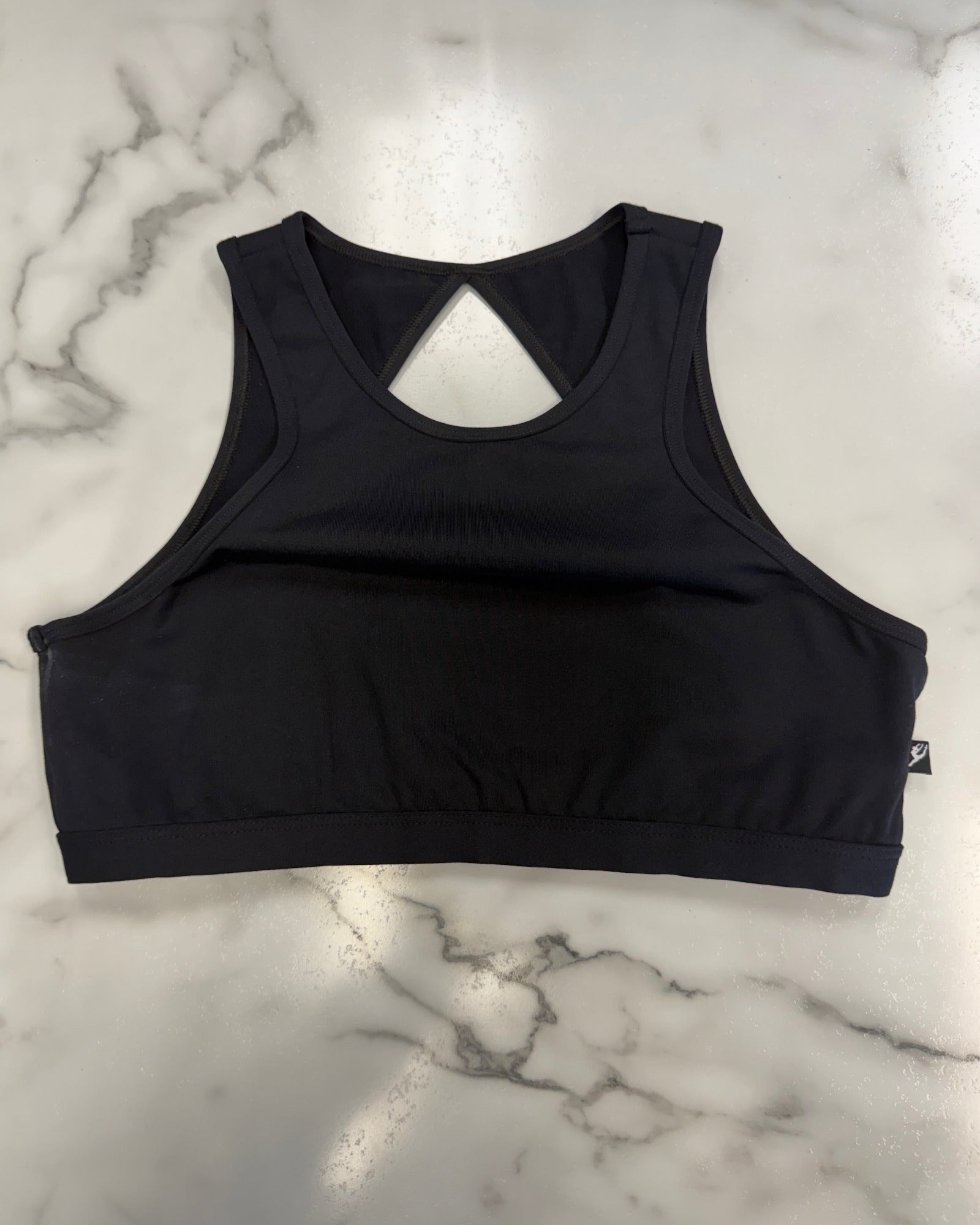 A black dance bra top with a keyhole cutout at the back, laid flat on a white marble surface.