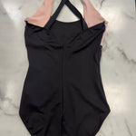 A black one-piece leotard with light pink shoulder straps, laid flat on a white marble surface.