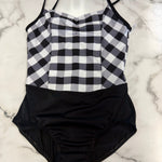 A leotard laid flat on a white marble surface. The top portion features a black and white gingham check pattern, while the bottom portion is solid black.