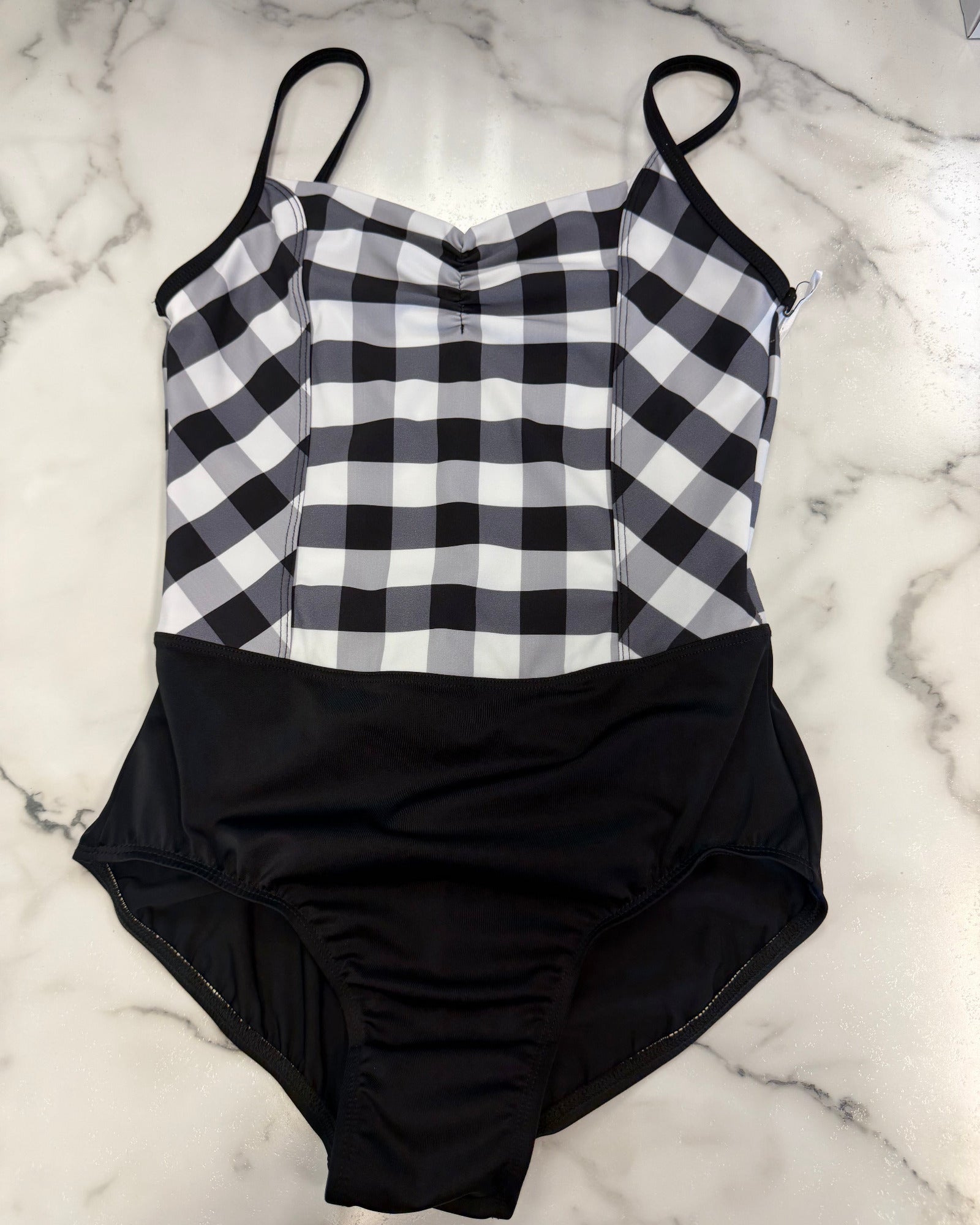 A leotard laid flat on a white marble surface. The top portion features a black and white gingham check pattern, while the bottom portion is solid black.